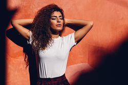 Arab woman with curly hair standing in the sun with her eyes closed and arms up