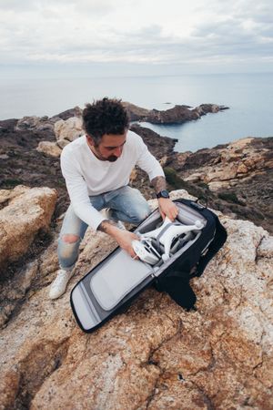 Man opening bag with drone equipment on a seaside cliff