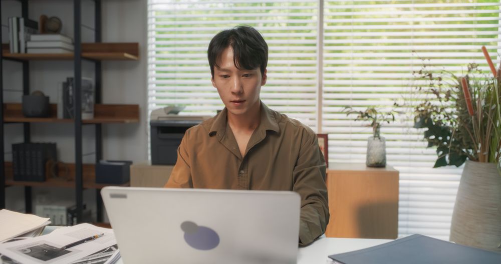 Young South Korean Professional, Immersed in Laptop Computer Work Behind a Desk at His Cozy Home Office