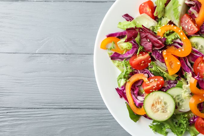 Plate with fresh salad on wooden background, space for text