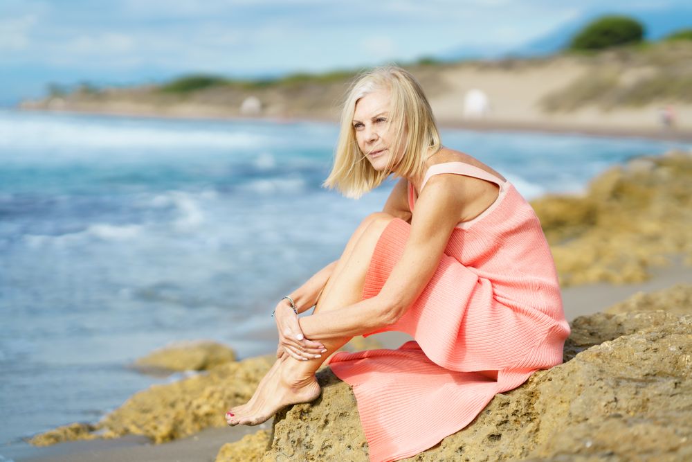 Serene older female with grey hair sitting on coastal rocks enjoying the view