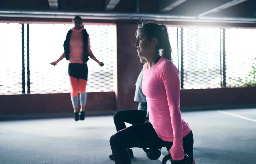 Side view of two woman doing squats with kettlebells