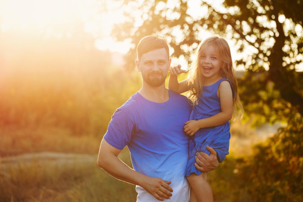 Dad holding daughter on his hip in sunny meadow