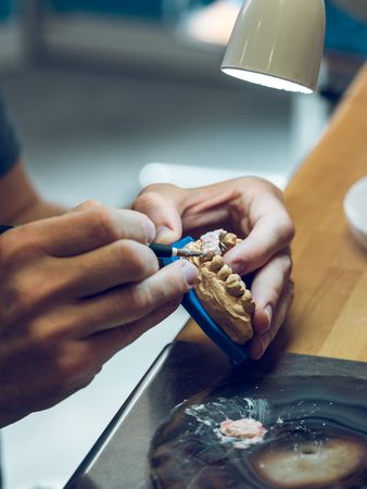 Unrecognizable technician applying paint on dental prosthetics