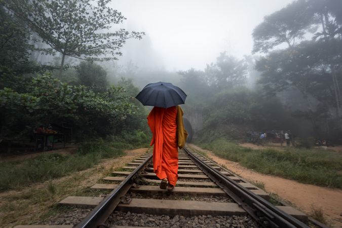 Person walking on train tracks holding dark umbrella