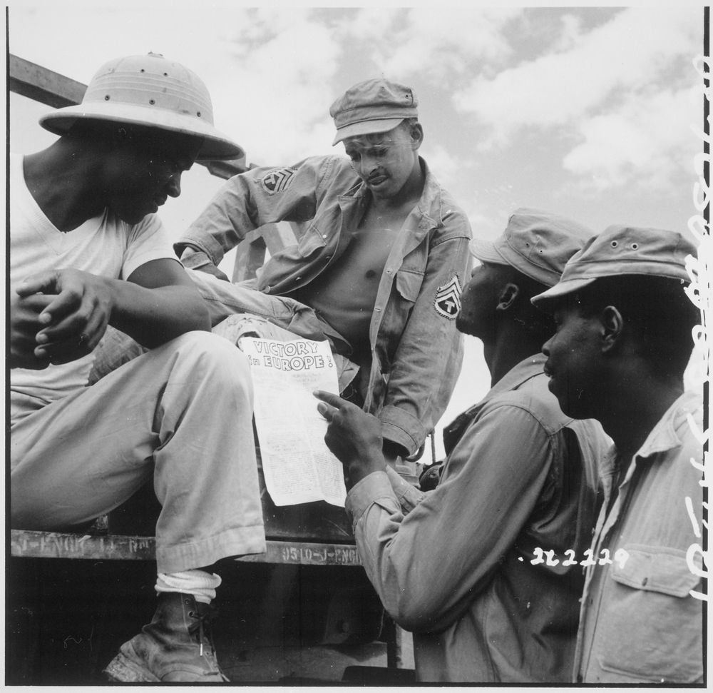Black American soldiers reading “Victory in Europe” sign in World War II