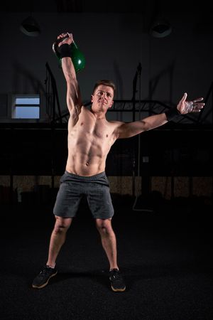 Sporty guy doing exercise with kettlebell in dark fitness club
