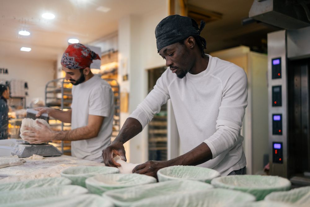 Black baker kneading in bakery with colleague