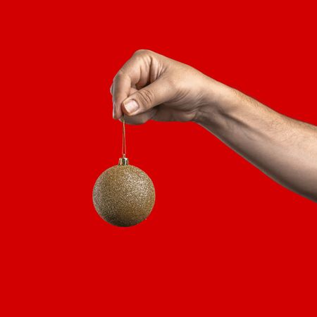 Hand holding a gold glitter Christmas bauble on a red background.