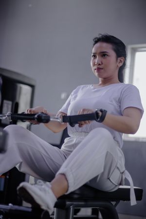 Dedicated young woman strengthening core muscles with rowing mac