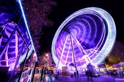 Purple lit ferris wheel with families walking around park