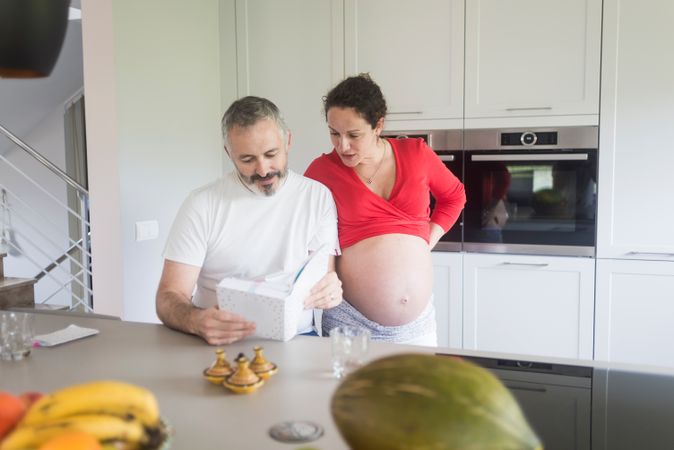 Pregnant woman and male partner reading recipe book together in bright kitchen