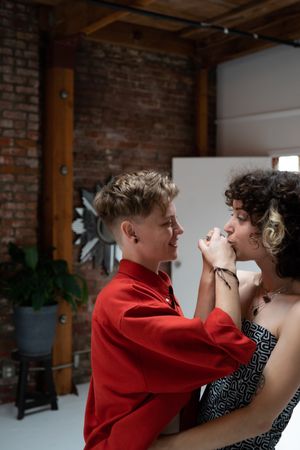 Woman with short curly hair holds her partner’s hand to her mouth for a kiss