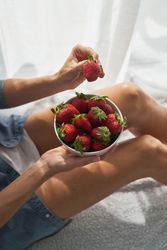 Unrecognizable female taking strawberry from bowl while sitting