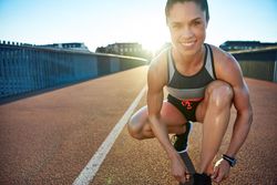 Smiling athletic woman leaning down on bridge tying her shoes