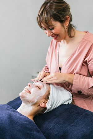 Crop beautician cleansing face of woman in salon
