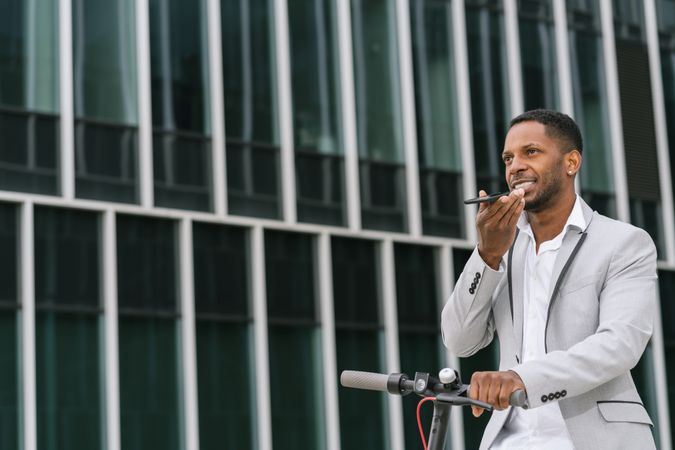 Smiling Black man riding scooter and speaking on smartphone
