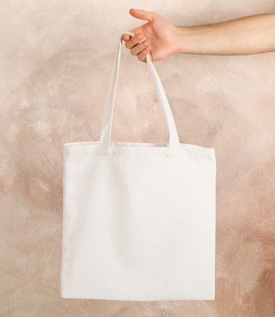 Male hand holding tote bag against brown background, empty space