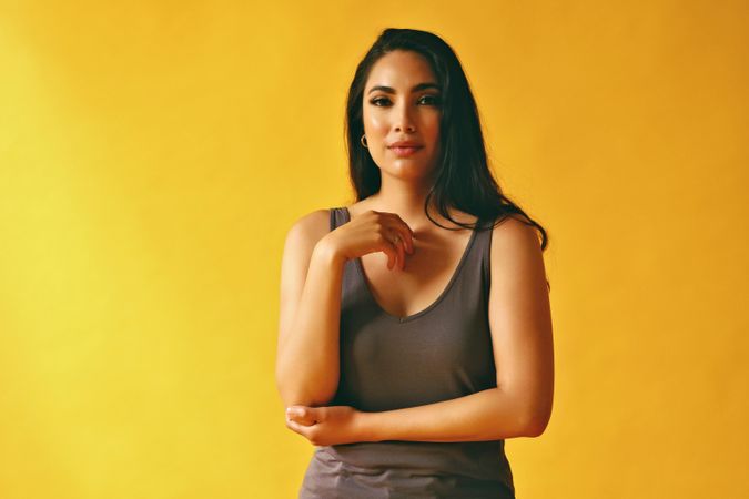 Serious Hispanic woman standing and looking at camera with hand to her chest in yellow room