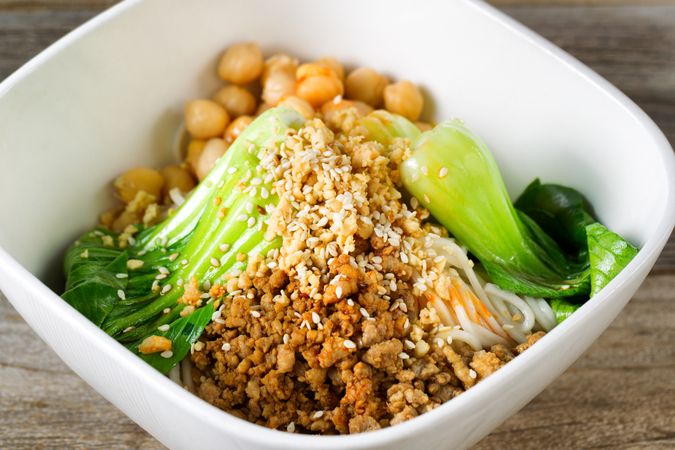 Spicy chicken and noodles in bowl on rustic wood