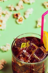 Popcorn on table near drink in glass with ice and lemon