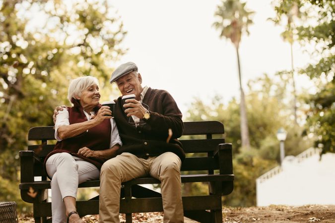 Older couple in seasonal fall clothing toasting each other with coffee on a date in the park