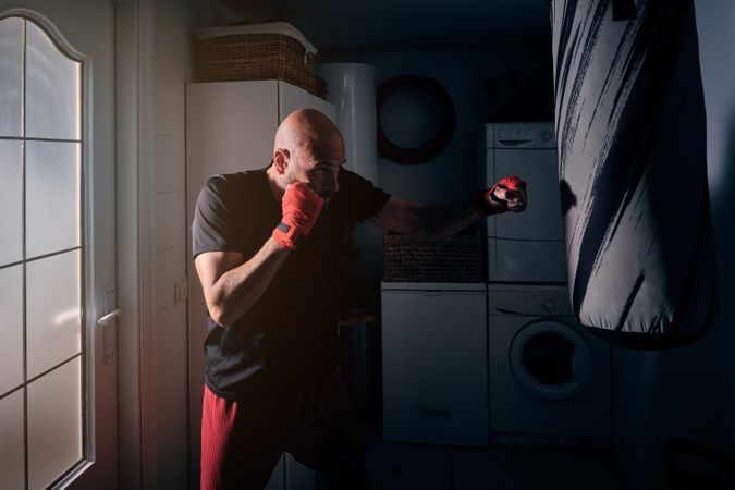 Man training boxing in the laundry room at home with a bag