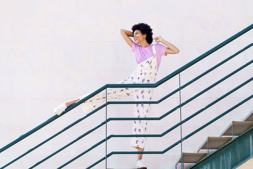 Woman on stairs with leg up on green handrail and arms on hair