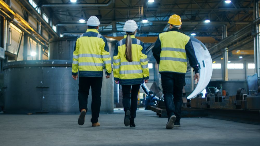 Following Shot of Three Engineers Walking Through Heavy Industry Manufacturing Factory.