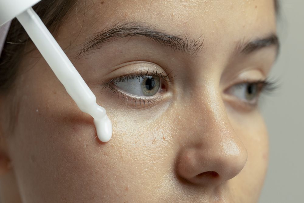 Close-up of young woman applying serum drop on natural skin texture with visible pores and healthy glow