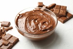 Bowl with chocolate and chocolate pieces on light background