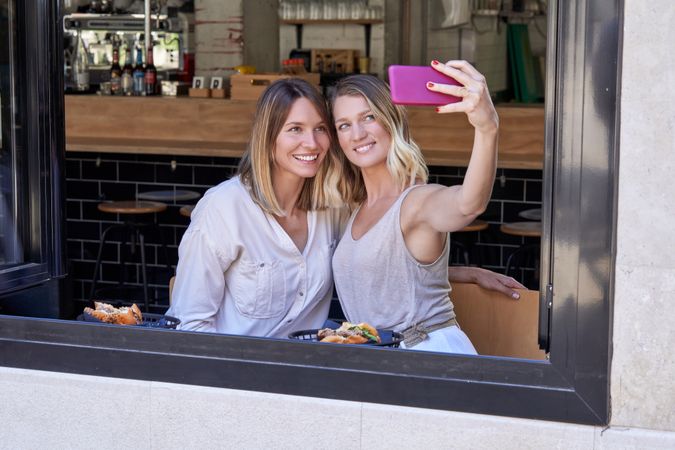 Smiling girlfriends taking self portrait on cellphone in restaur