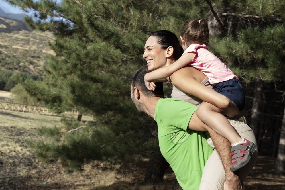 Family playing outdoors with child on mom’s back and dad supporting togetherness
