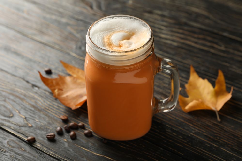 Glass jar of pumpkin latte, coffee seeds and leaves on wooden background