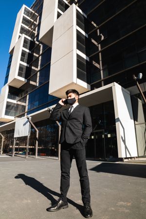 Businessman in mask speaking on smartphone in city