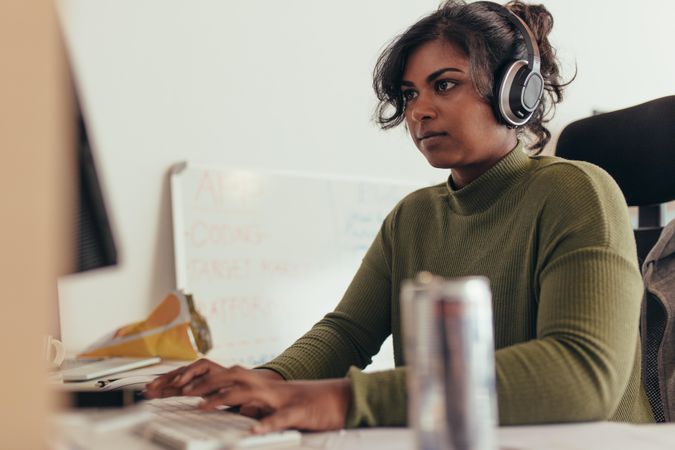 Woman wearing headphones coding on desktop computer