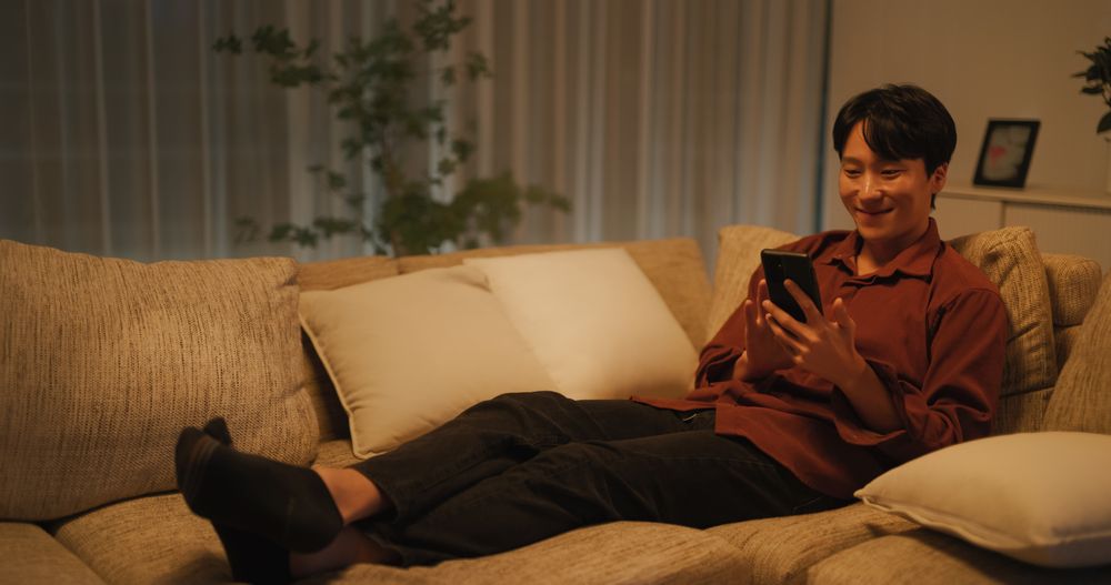 South Korean Young Man Enjoying His Leisure Time while Relaxing and Using a Smartphone.