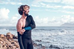 Content muscular male surfer putting wetsuit on