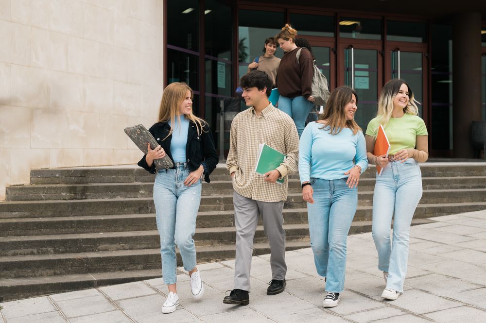 Happy young friends walking near university building after studies