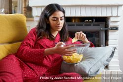 Female in red pajamas lying on sofa and snacking on chips 43Wyx4