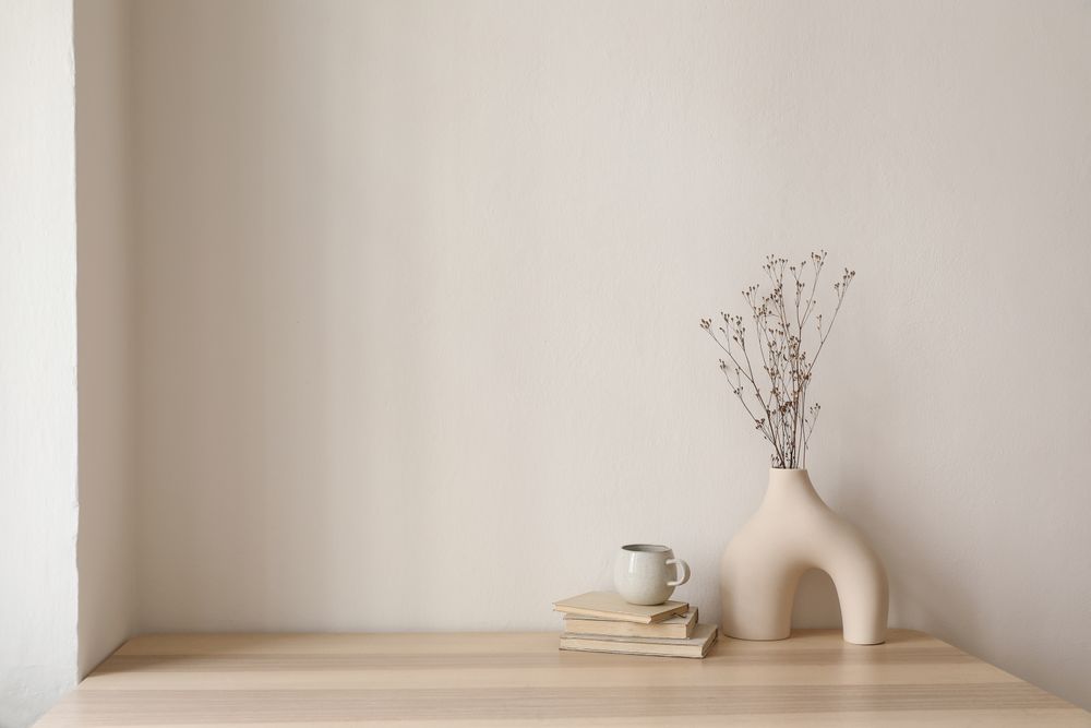 Table with modernist vase and decorative reeds, and coffee atop pile of books