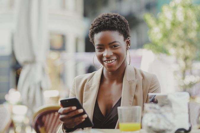 Smiling Black woman with smartphone sitting at table in cafe