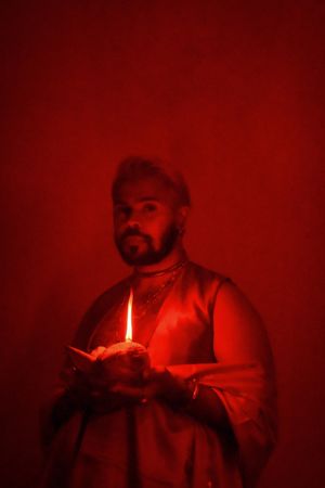 Man in red lit room holding a candle celebrating Diwali
