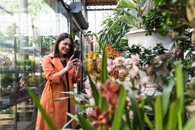 Content woman taking photo of flowers in garden center