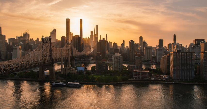 Evening New York City Landscape Over East River with Upper East Side Skyscrapers and Ed Koch Queensboro Bridge. Cinematic Urban Skyline with Sunset and Lightly Clouded Sky