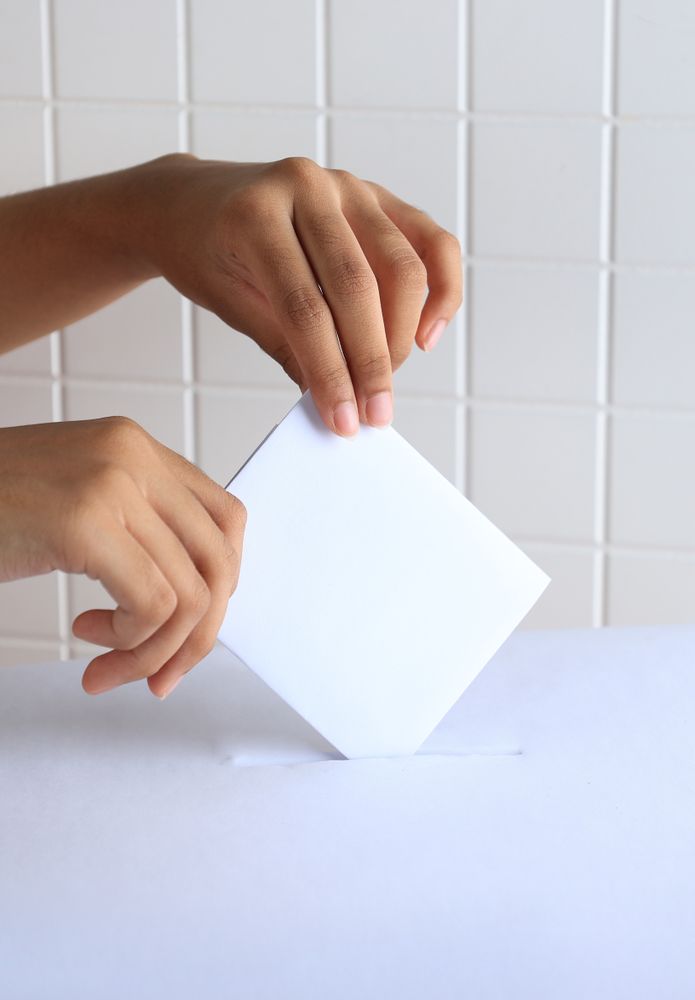 Female Hand Lowers Ballot In Ballot Box