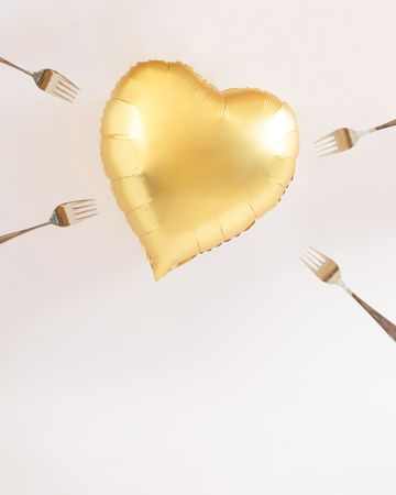 Heart balloon gold surrounded with forks trying to poke it