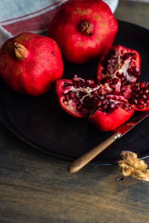 Dark bowl full of fresh whole pomegranates with knife