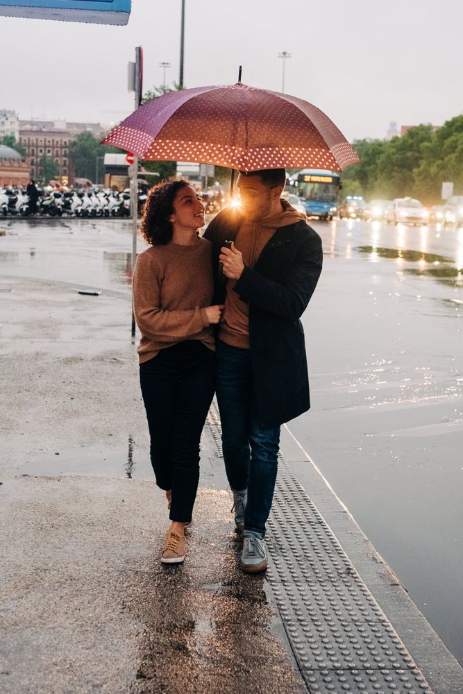 Happy couple with umbrella hugging on wet street