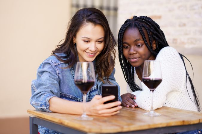 Female friends looking at smart phone at a restaurant with red wine